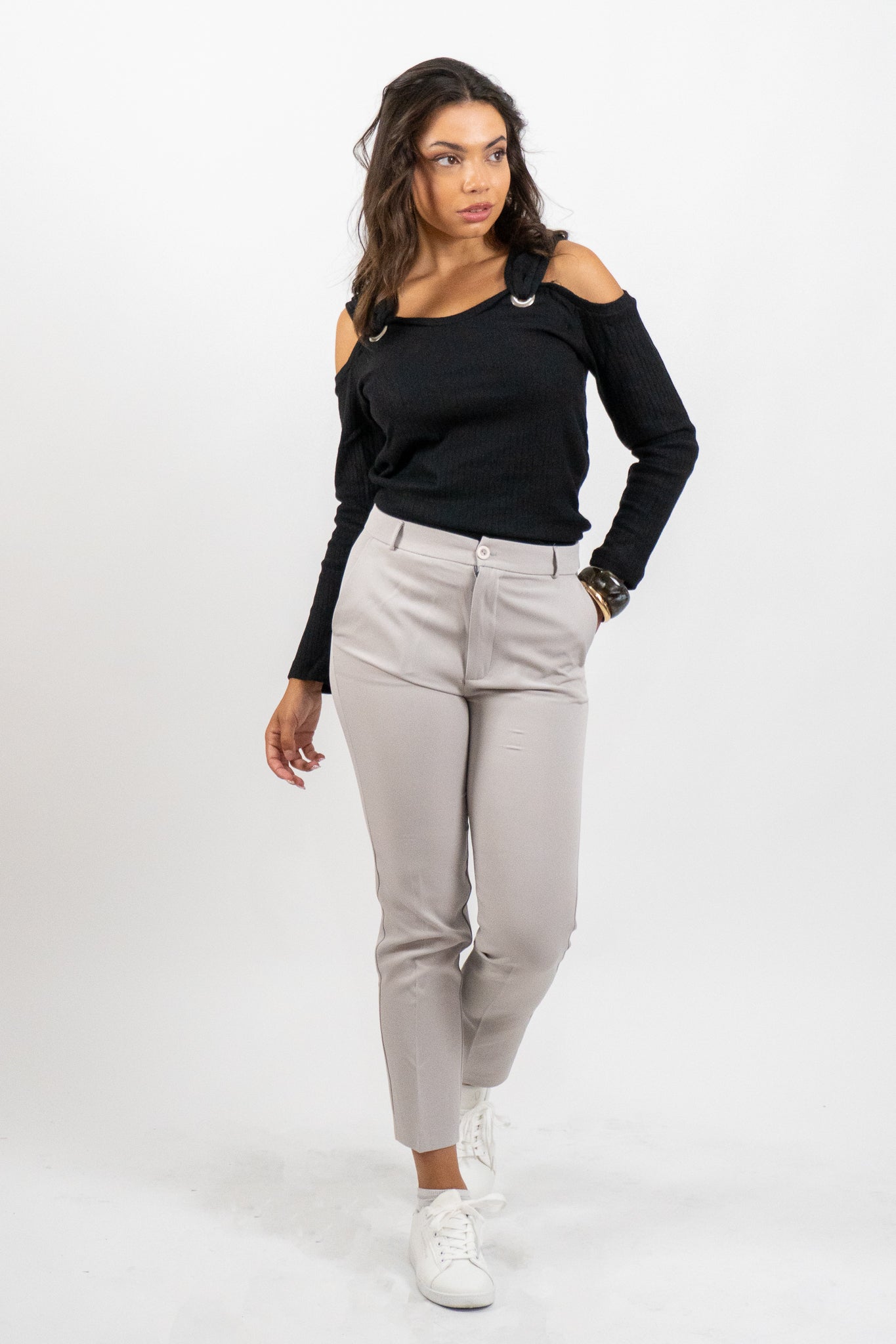 Woman wearing a black off-shoulder top and beige pants on a white background