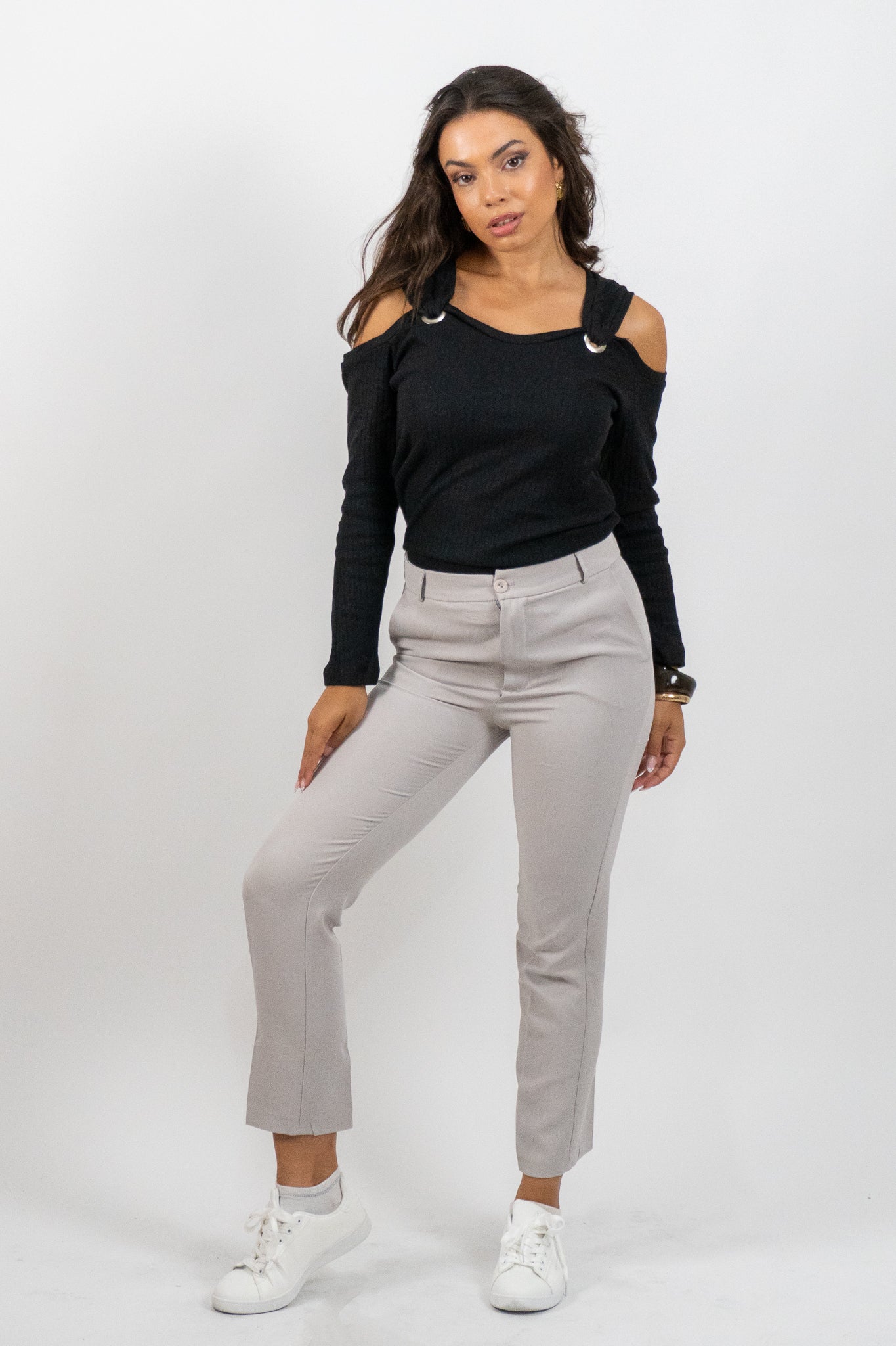 Woman wearing a black long-sleeve top and light gray pants on a white background