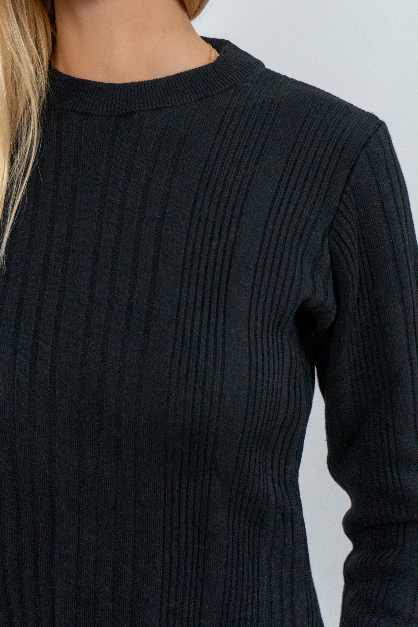 Black ribbed sweater worn by a person on a light gray background