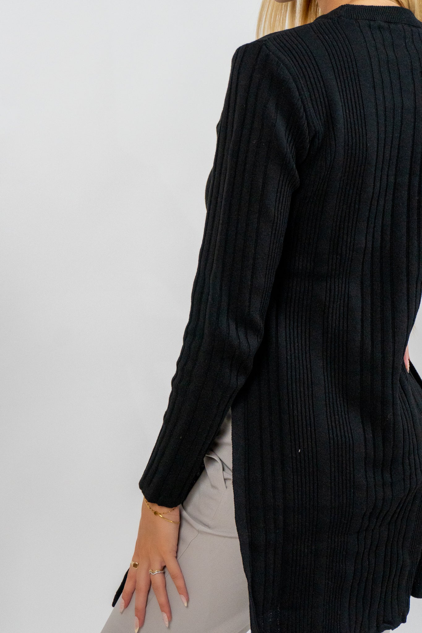 Person wearing a black ribbed cardigan against a plain background
