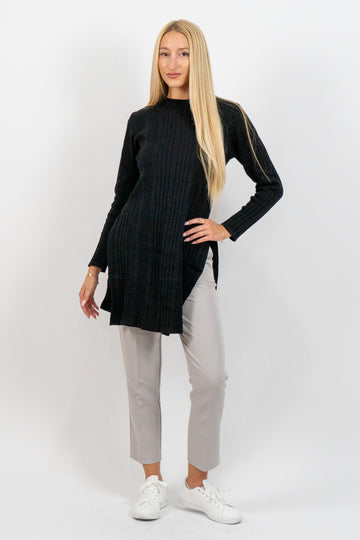 Woman wearing a black long-sleeve top and light gray pants on a white background