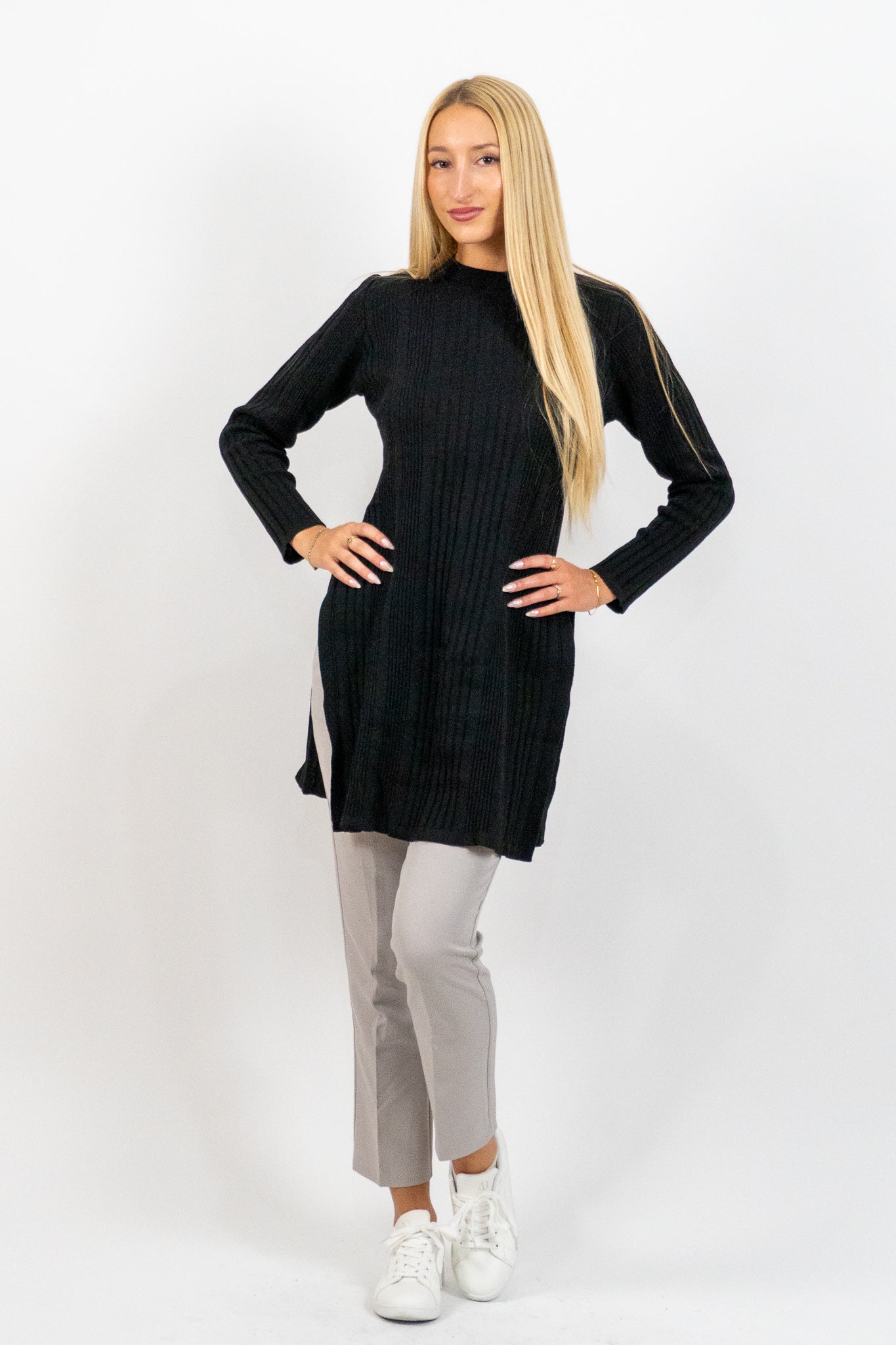 Woman wearing a black long-sleeve dress over gray pants on a white background