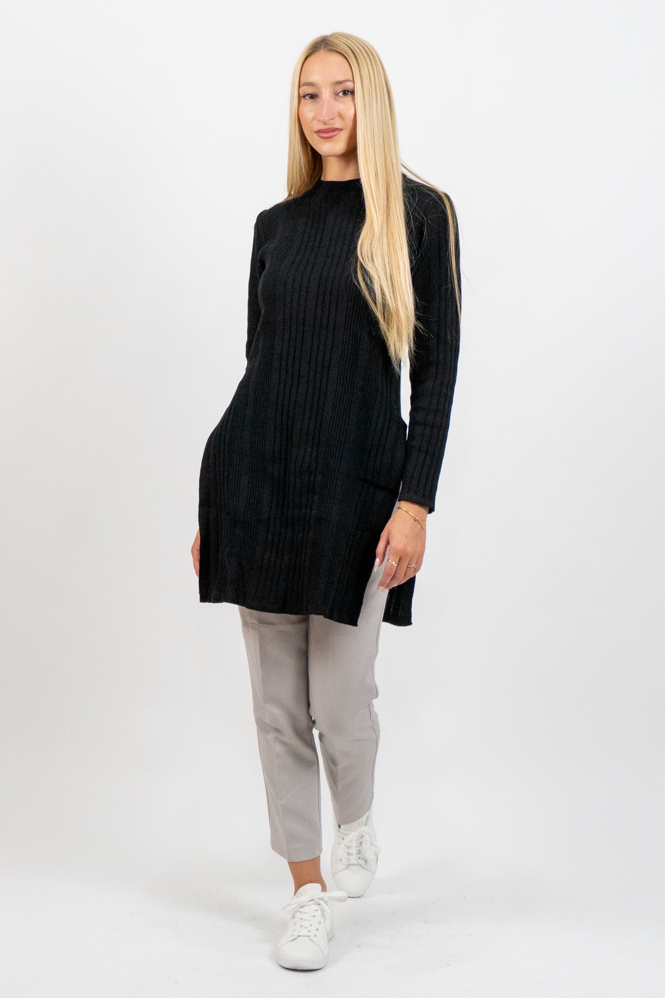 Woman wearing a black long-sleeve dress with gray pants and white sneakers on a white background