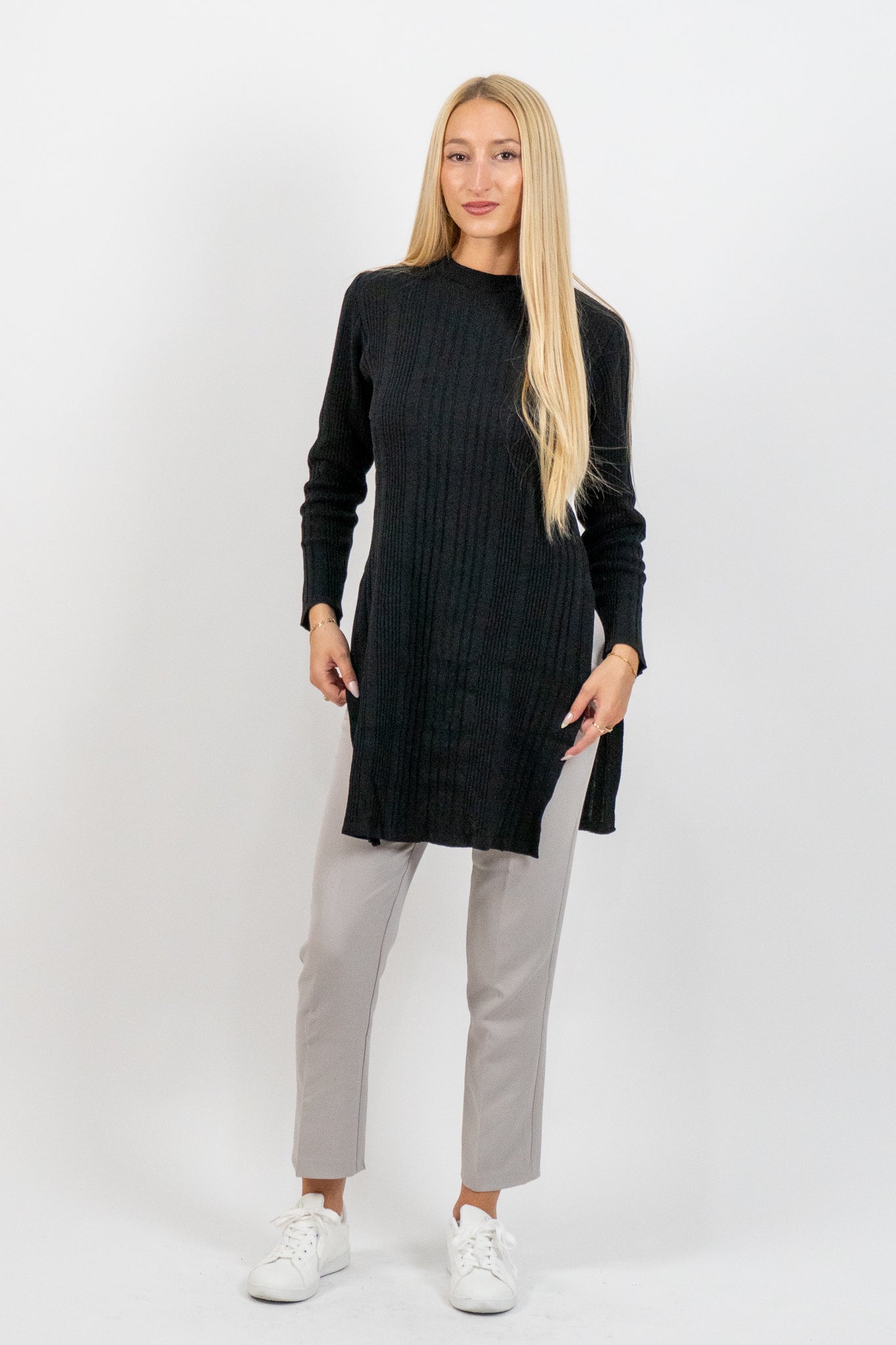 Woman wearing a black long-sleeve top and light gray pants on a white background