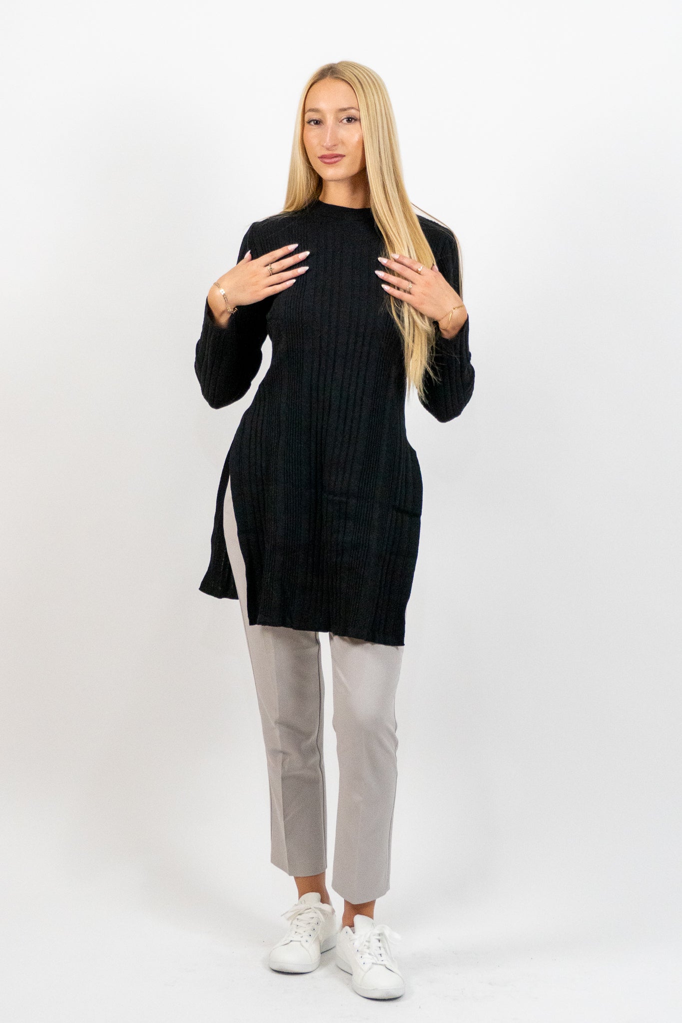 Woman wearing a black long-sleeve top and light gray pants on a white background