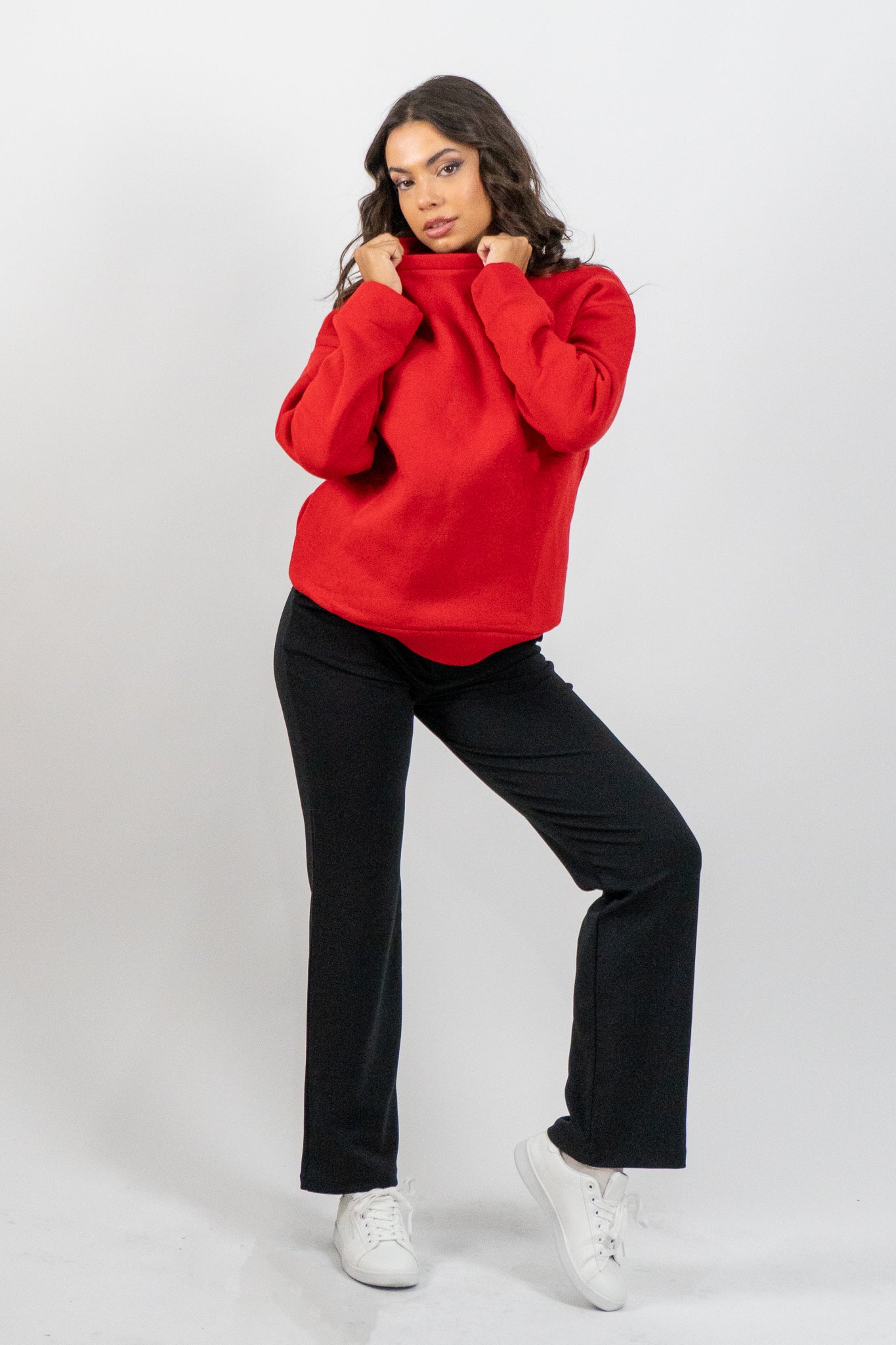 Woman wearing a red sweater and black pants on a white background
