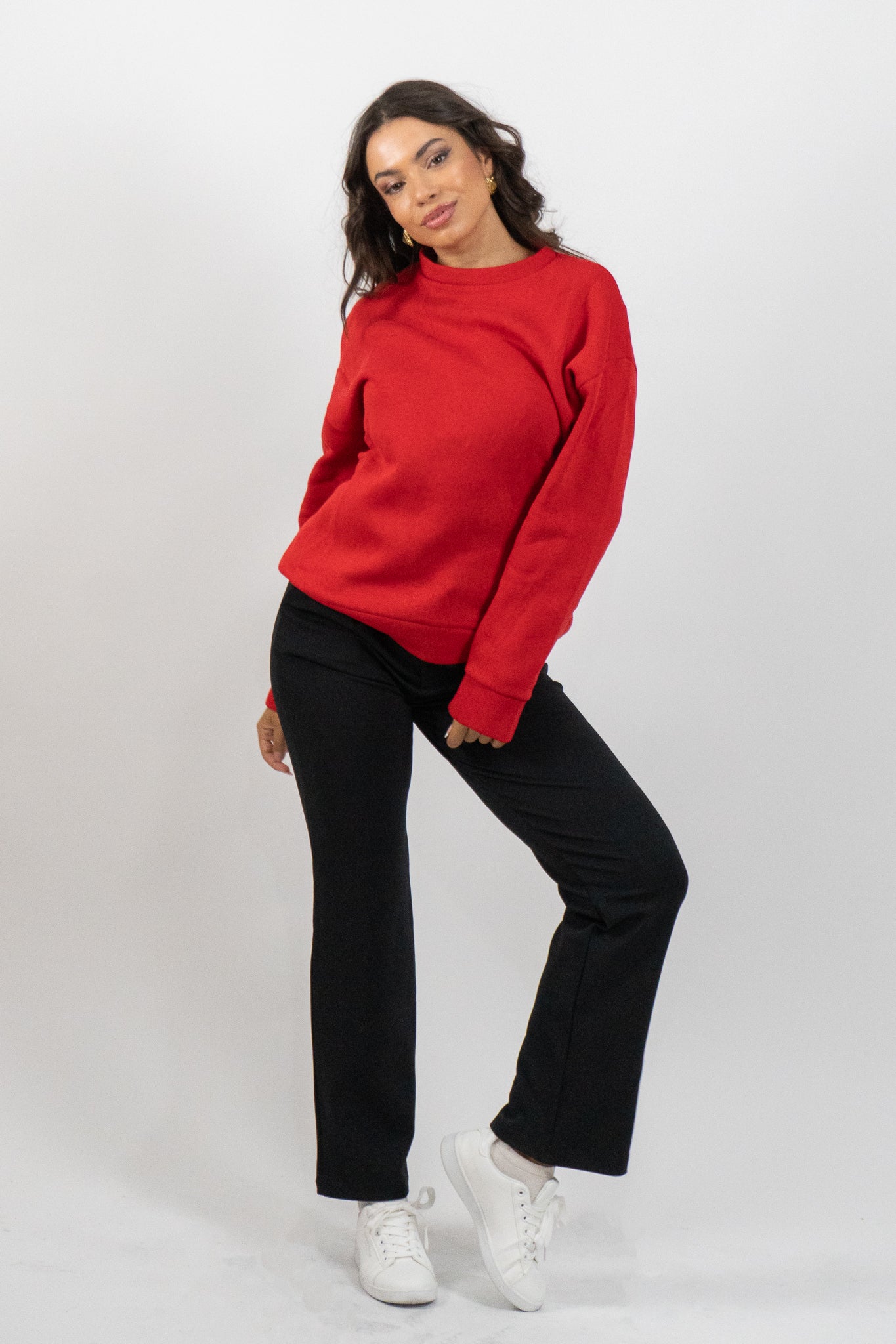Woman wearing a red sweater, black pants, and white sneakers on a white background
